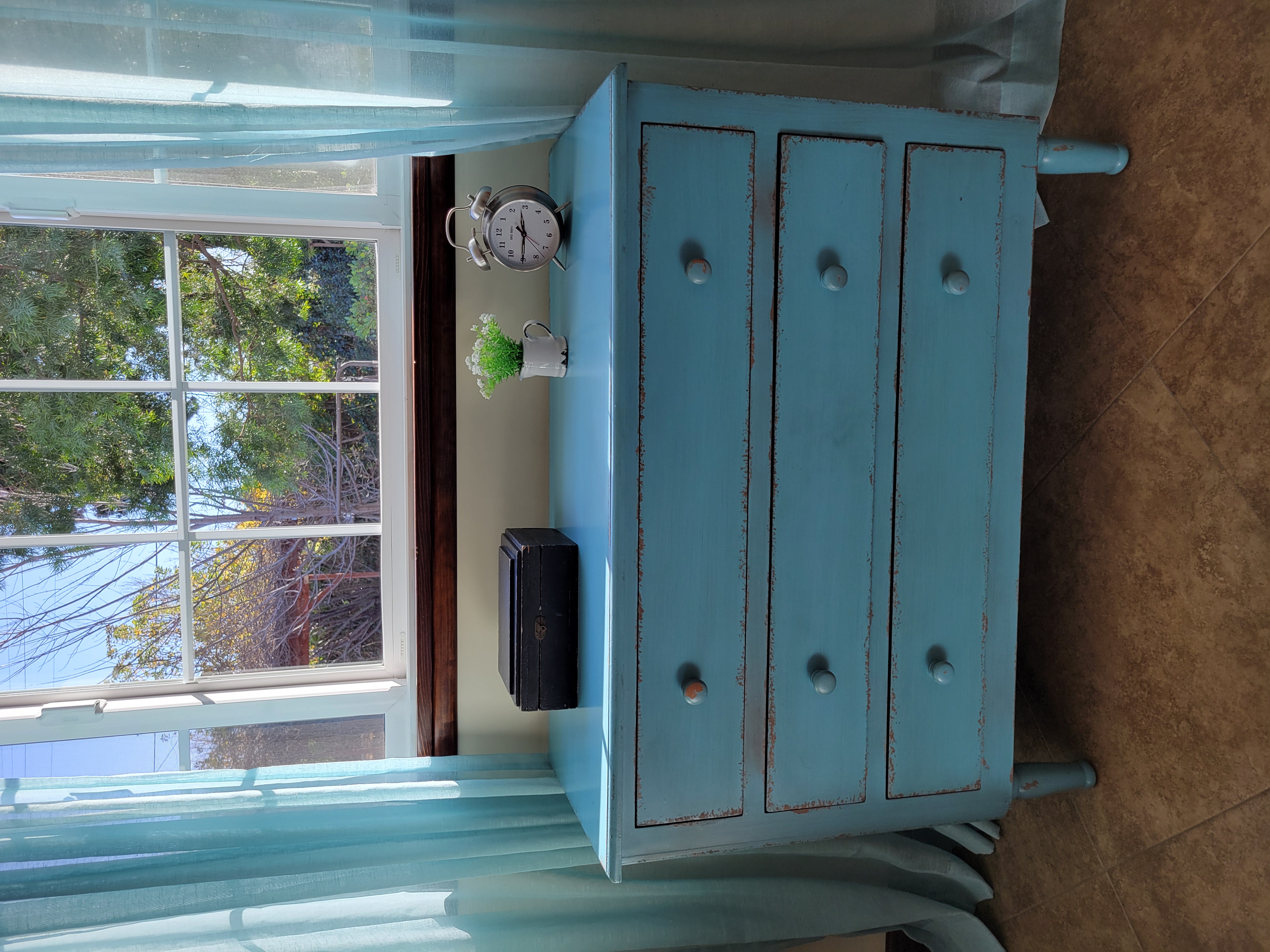 Bureau drawers chipped paint under window blue gauze drapes